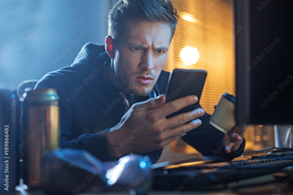 Poster portrait of orderly male sending message by smartphone while tasting coffee. he working at table wit