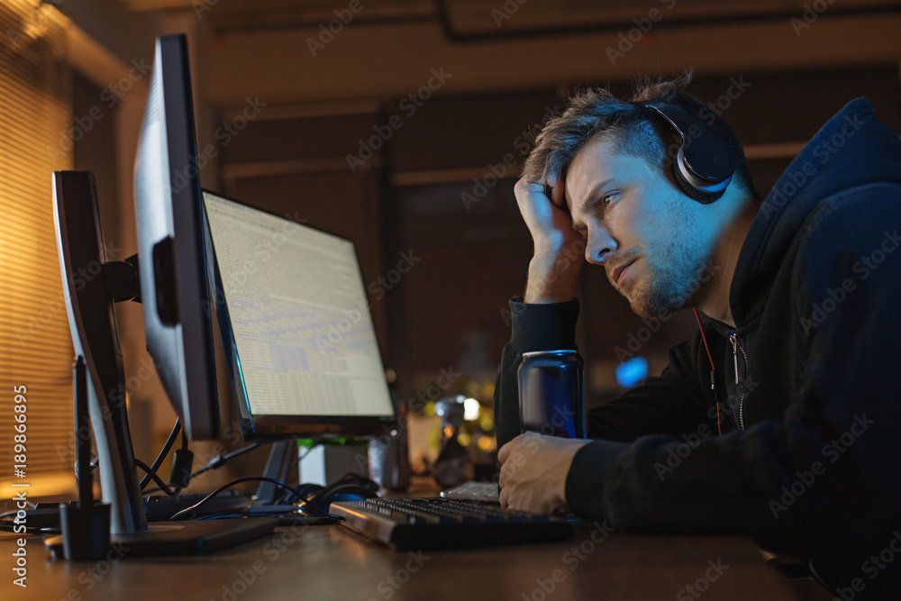 Poster side view calm programmer looking at screen of gadget while listening music. he tasting can of energ