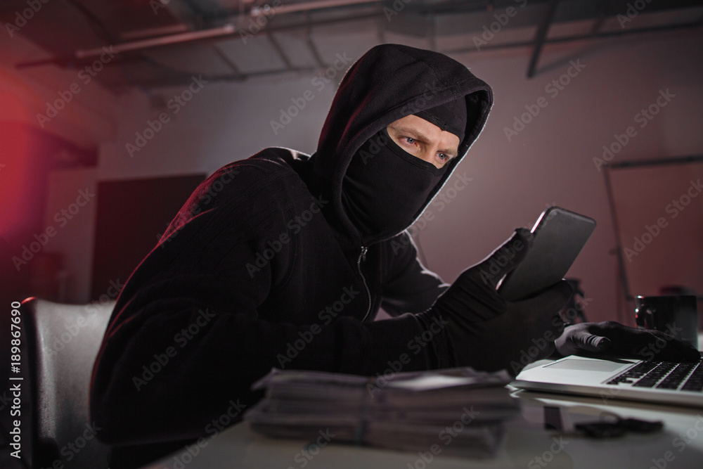 Poster portrait of serene hacker looking at mobile while situating at desk in apartment. technology and ste