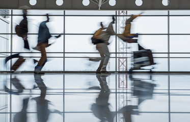 Travel concept. Blurred terminal lounge with running tourists. Man is pushing airport trolley with...