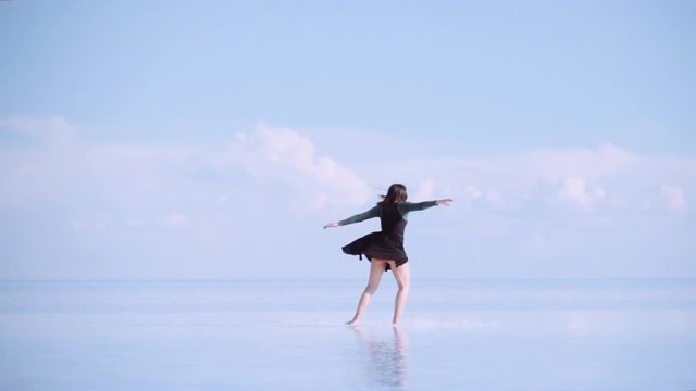 Happy woman dances wearing a black dress on the salt flats of Uyuni, Bolivia. Reflex in the water of the landscape doing a mirror effect. Slow motion