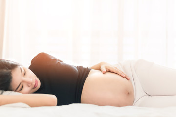  Pregnant woman touching her belly and lying on the bed in  bedroom.