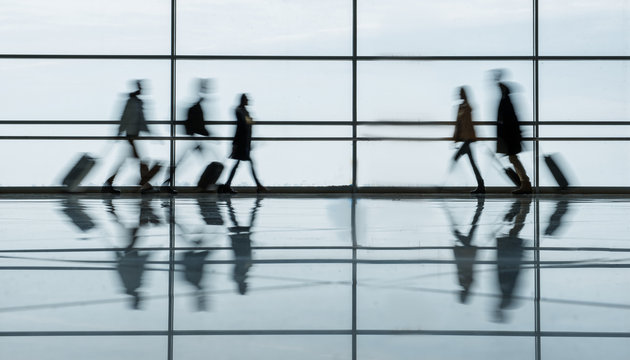 Defocused airport hall with walking travelers. They are going toward to each other in terminal lounge with luggage. Travel concept. Full length