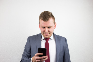 Young and handsome businessman in suit writing text message to his colleagues about business idea and plan. Light smile on the face with joy of success.