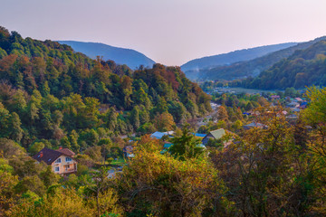Landscape of Plastunka village in the valley and mountains with varicolored trees in sunny autumn day, Sochi, Russia
