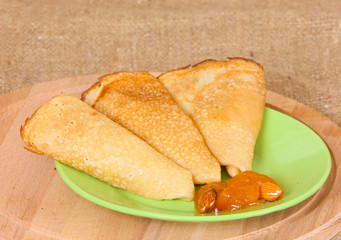 Fried pancakes folded in a triangle with apricot jam lie on a green plate and a wooden cutting board. The concept of making sweet pastries. Horizontal image.