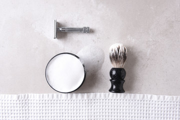 Obraz premium Safety razor with towel, brush and soap on a gray tile surface