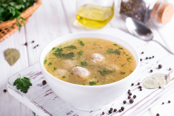 Soup with chicken meatballs and vegetables on white wooden background