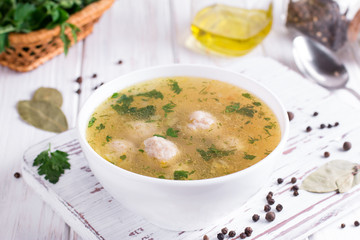 Homemade soup with chicken meatballs and vegetables on white wooden background