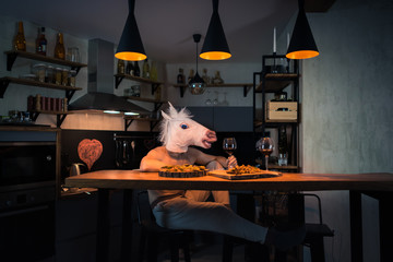 Young man sitting at the table with food and drinking wine in modern home kitchen. Funny unicorn...