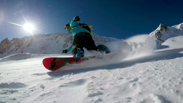 snowboarder make snow splash on slope at sunny winter day