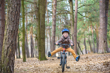 Plakat Happy kid boy of 3 or 5 years having fun in autumn forest with a bicycle on beautiful fall day. Active child wearing bike helmet. Safety, sports, leisure with kids concept.