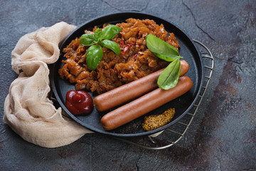 Stewed cabbage and sausages served on a metal tray, grey cracked background, studio shot