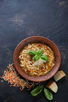 Italian soup with red lentil, pasta and addition of parmesan over dark brown stone background, high angle view with copyspace, vertical shot