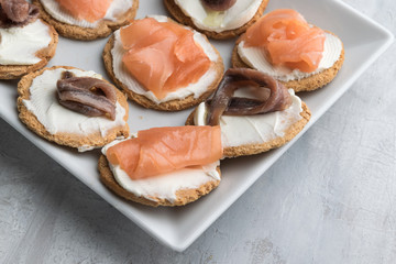 Homemade canapes with smoked salmon, anchovies and cream cheese. Lifht gray background. Copy space.