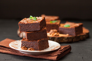 Chocolate brownie square pieces in stack on white plate with walnuts, decorated with mint leaves...