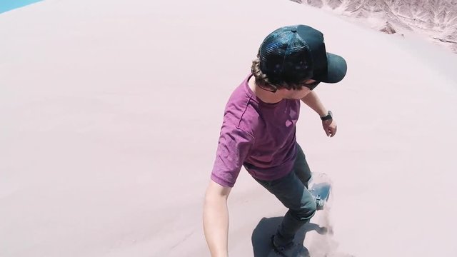 Young man sandboarding over great Sand Dunes of the Dead Valley, Atacama desert. Man using an action camera when slide on a sandboard.