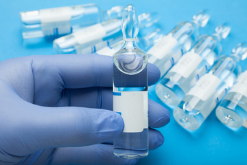 Close-up, ampoule in doctor's hand on blue background.