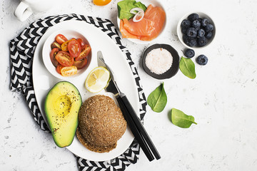 Healthy breakfast: cereal rolls with salmon, cherry tomatoes, spinach, avocado. blueberry on a light background. Top view. Copy space.
