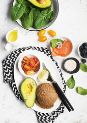 Healthy breakfast: cereal rolls with salmon, cherry tomatoes, spinach, avocado. blueberry on a light background. Top view. Copy space.