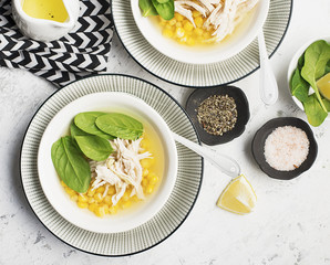 Fresh homemade chicken soup broth with corn, spinach, boiled breast on a light background. Top view. Copy space.