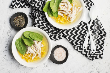 Fresh homemade chicken soup broth with corn, spinach, boiled breast on a light background. Top view. Copy space.