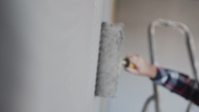 Painting out a bare wall with a paint roller with gray paint. Hand painting using paint roller. Painter girl at work, with roller painting wall, painter house concept