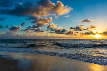 yellow and blue sky reflecting off the wet sand and ocean waters at sunrise