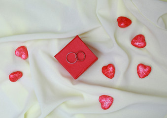 On the red box on the background of bright silk are two wedding rings and hearts