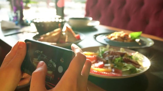 Girl makes a photo of meal on a smartphone in a cafe close up
