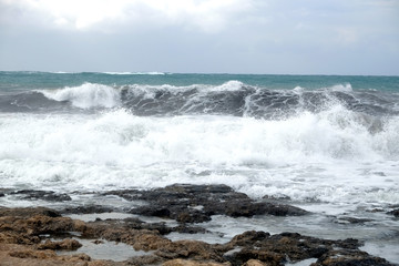 Fototapeta na wymiar Sea waves break about the coastal stones during the storm, the splashes of white foam fly upward front view