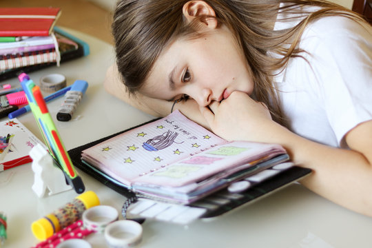 Beautiful preteen girl daydreaming with her head lying on hands looking at her romantic diary. Close-up