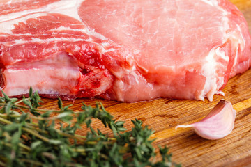 Raw pork natural cutlet with a bunch of thyme and a slice of garlic on a wooden cutting board close-up