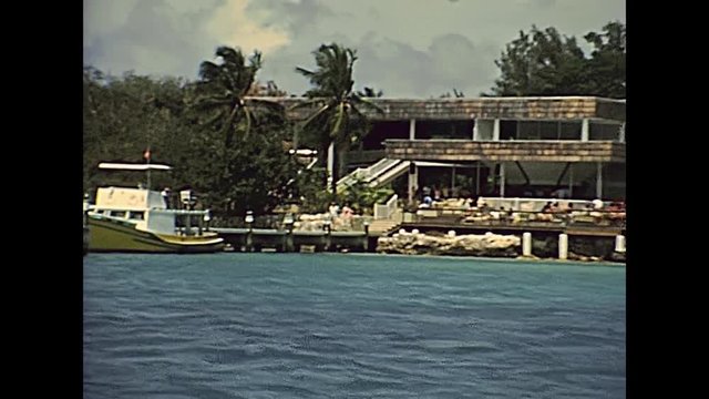 Waterfront cruise from Nassau to Paradise Beach through coastline and ports with fishing boats and hotels in 70's with old buildings. The historical Bahamas in 1978.