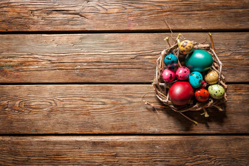 colored chicken and quail eggs in a small nest on wooden background for Holy festival of Easter