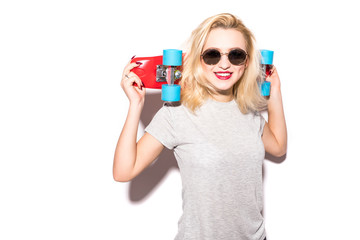 Portrait of a cheerful young woman holding skateboard while standing and looking at camera over white background