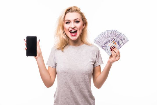 Picture of shocked young woman standing Looking camera holding money showing display of mobile phone isolated over white background.