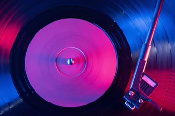 A retro-styled spinning record vinyl player. Vintage shot of old gramophone, playing close up. Beautiful colorful movie. Neon violet led light.
