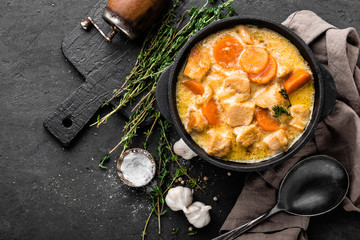 Meat stew, chicken fillet in sauce with carrot in a cast iron pot, top view