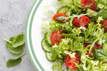 Healthy vegetable salad of fresh tomato, cucumber, spinach, frize and sesame on plate. Diet menu. Top view.