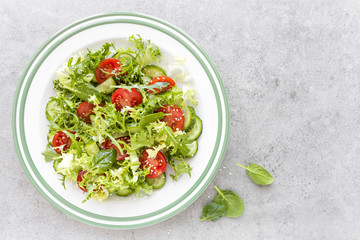 Healthy vegetable salad of fresh tomato, cucumber, spinach, frize and sesame on plate. Diet menu. Top view.