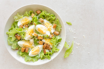 Caesar salad with eggs, lettuce and parmesan cheese on plate. Top view