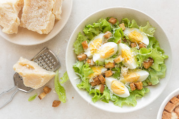 Caesar salad with eggs, lettuce and parmesan cheese on plate. Top view