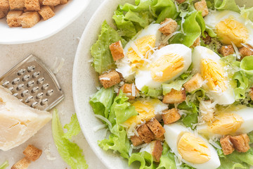 Caesar salad with eggs, lettuce and parmesan cheese on plate. Top view