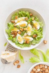Caesar salad with eggs, lettuce and parmesan cheese on plate. Top view