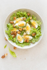 Caesar salad with eggs, lettuce and parmesan cheese on plate. Top view