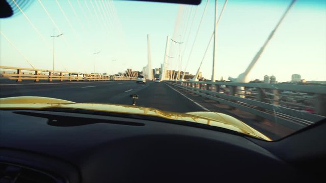 Middle aged man is driving his luxurious yellow cabriolet moving along the Golden Bridge across the Golden Horn harbour in the morning. Vladivostok, Russia