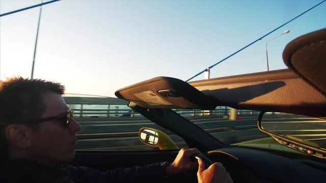 middle aged man in sunglasses is driving fancy yellow cabriolet at sunrise.