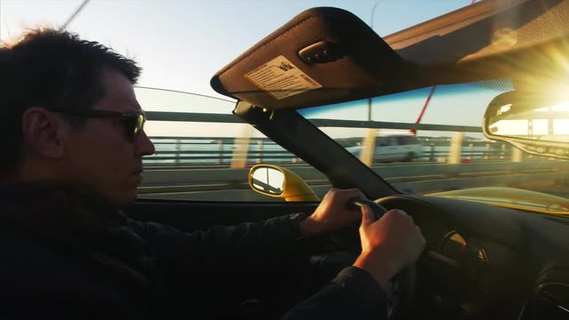 middle aged man in sunglasses is driving fancy yellow cabriolet at sunrise.