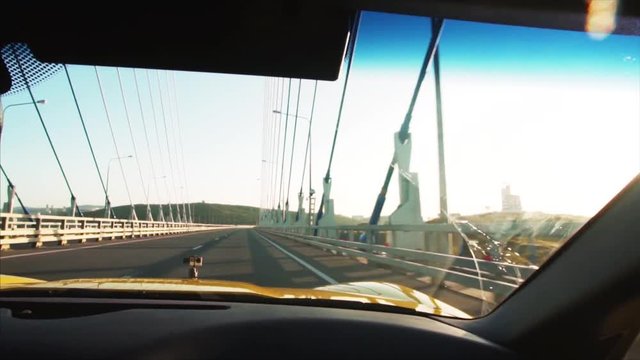 View of the road from the side mirror of yellow cabriolet driving along Russian bridge that connects the mainland part of Vladivostok with Russian Island